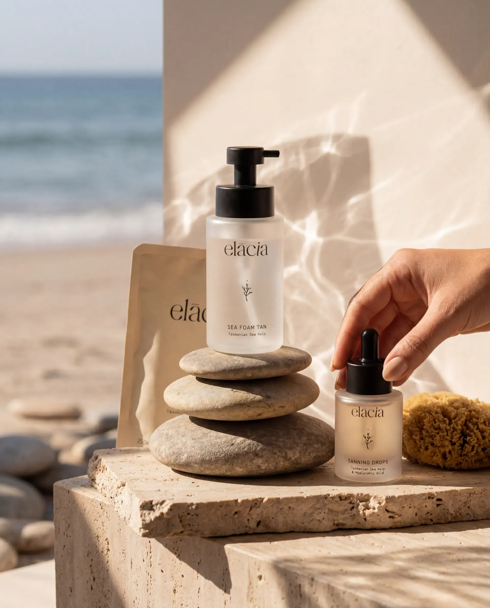 Elacia bottles on stacked beach stones by the sea, a hand placing a dropper
