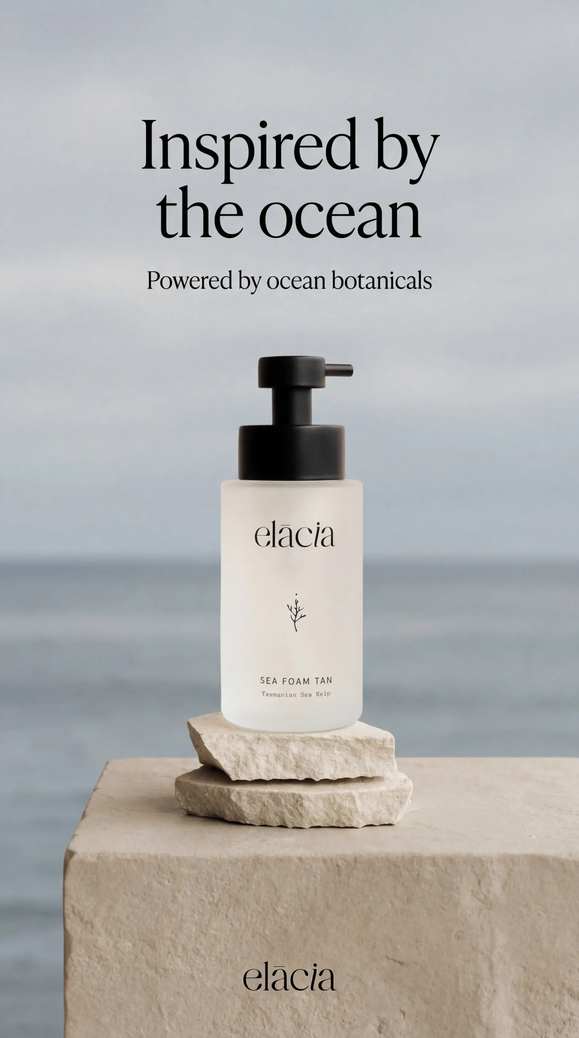 Finished Elacia story ad: “Inspired by the ocean”, a Sea Foam Tan bottle on a stone plinth by the sea.