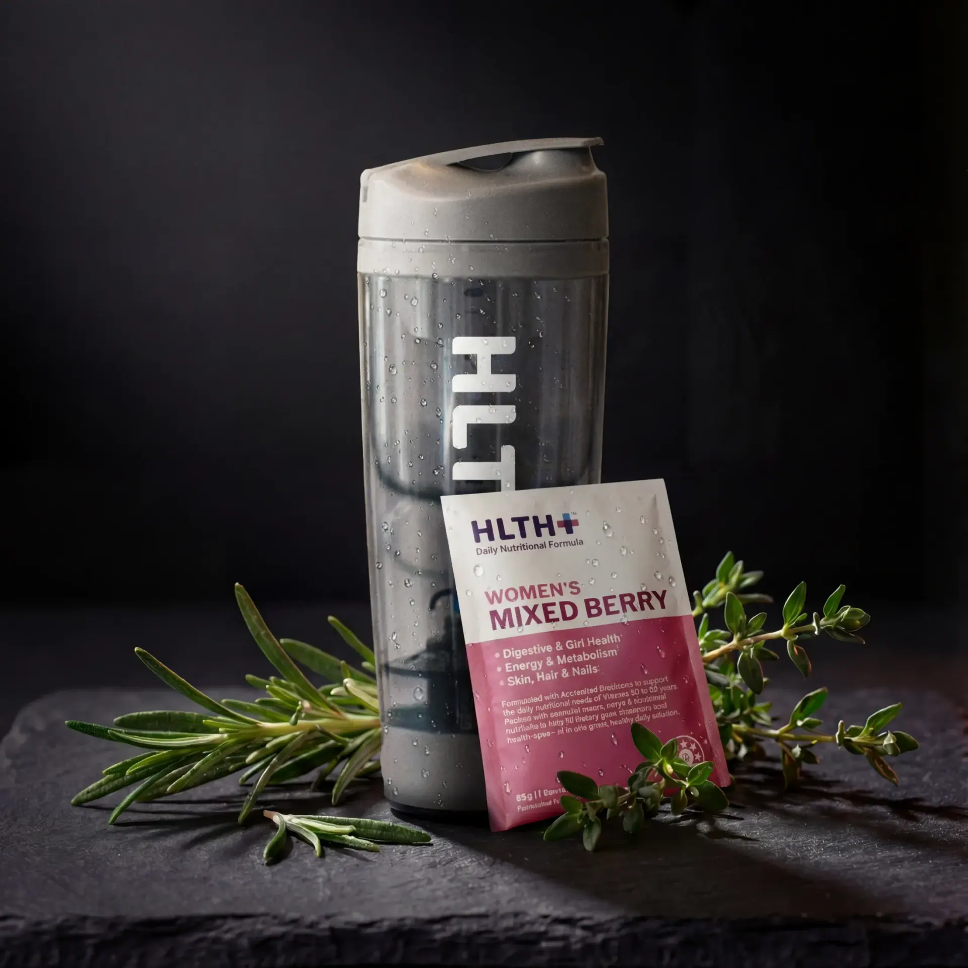 Hlth+ shaker and a Women's Mixed Berry sachet on slate with fresh herbs.